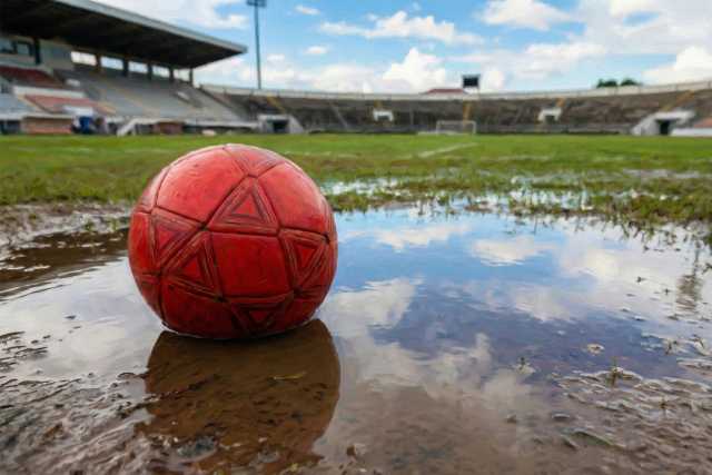 red-soccer-ball-by-puddle-muddy-stadium-pitch